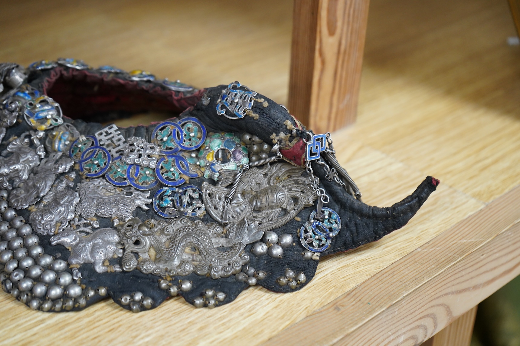 A Chinese Zhuang silver and enamel ceremonial hat, Yunnan Province. The hat heavily covered with auspicious silver and silver enamel charms for good luck and prosperity with a tail/horn shape one side and large silver fl